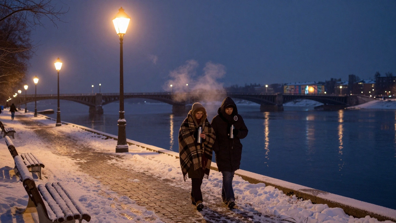 Двое гуляют по зимней набережной под пледом, пар поднимается от термоса, свет фонарей отражается в реке.